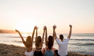 Quatro pessoas em frente ao mar com mãos levantadas