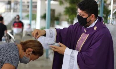 Padre, vestido com paramentos roxos, impõe cinzas na cabeça de uma fiel durante a celebração da Quarta-feira de Cinzas, rito que marca o início da Quaresma na Igreja Católica.