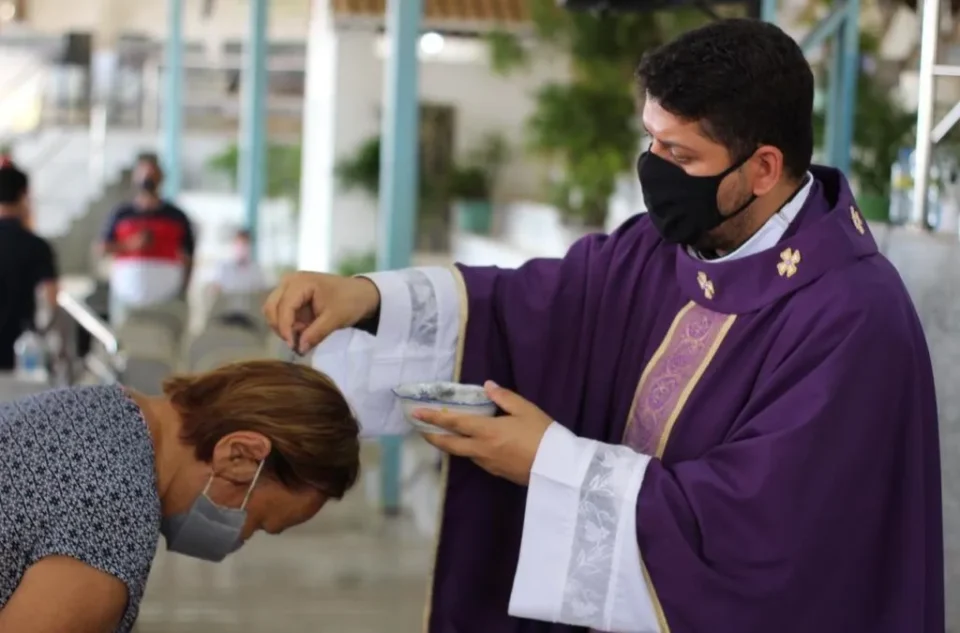 Padre, vestido com paramentos roxos, impõe cinzas na cabeça de uma fiel durante a celebração da Quarta-feira de Cinzas, rito que marca o início da Quaresma na Igreja Católica.