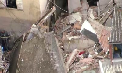 Escombros de uma casa destruída após possível explosão de gás na Brasilândia, zona norte de São Paulo. Entre os destroços, é possível ver partes da estrutura colapsada, objetos domésticos e moradores tentando resgatar pertences.