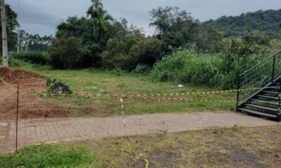Área isolada em Ivoti (RS) após ataque de abelhas durante cavalgada; fita de segurança delimita o local próximo a uma escadaria metálica, cercado por mata e vegetação densa.