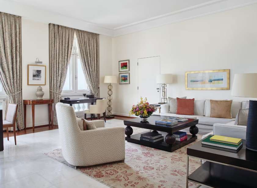 Sala de estar sofisticada da suíte presidencial do Copacabana Palace, decorada com móveis elegantes, tapete clássico, cortinas longas e arranjo floral sobre mesa de centro