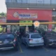 Fachada da padaria Natália, no bairro Serrano, em Belo Horizonte, com letreiro visível e vários carros estacionados em frente ao estabelecimento. Placa anuncia preços de marmitex.