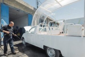 Homem lava o antigo papamóvel branco, adaptado com cobertura transparente e assentos, em oficina na Faixa de Gaza antes da transformação em unidade móvel de saúde infantil.