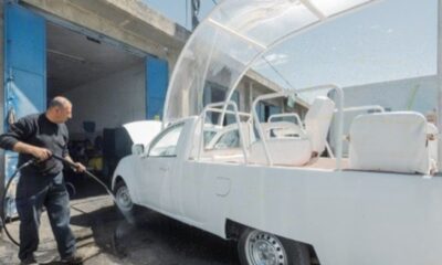 Homem lava o antigo papamóvel branco, adaptado com cobertura transparente e assentos, em oficina na Faixa de Gaza antes da transformação em unidade móvel de saúde infantil.