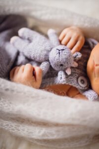 Mãos de bebê segurando um ursinho de pelúcia cinza