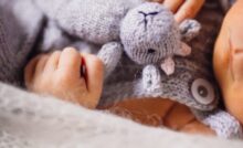 Mãos de bebê segurando um ursinho de pelúcia cinza