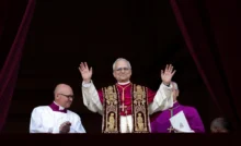 Novo Papa Leão XIV acena ao público da varanda da Basílica de São Pedro, acompanhado por membros do clero, durante sua primeira aparição oficial após eleição