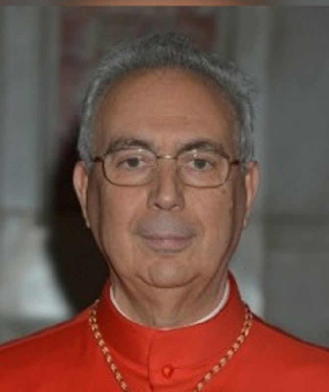Cardeal Dominique Mamberti, vestindo paramentos vermelhos e usando óculos, posando para foto em ambiente interno do Vaticano
