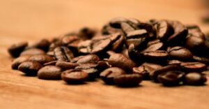 Grãos de café torrado espalhados sobre uma superfície de madeira, em close-up com fundo desfocado