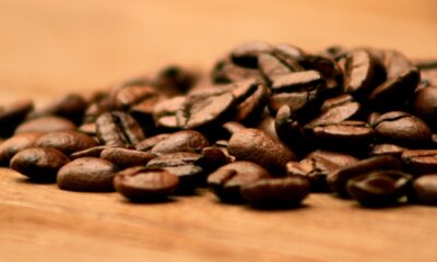 Grãos de café torrado espalhados sobre uma superfície de madeira, em close-up com fundo desfocado