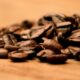 Grãos de café torrado espalhados sobre uma superfície de madeira, em close-up com fundo desfocado