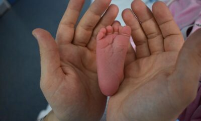 Mãos de um adulto seguram delicadamente o pé de um recém-nascido, simbolizando cuidado, proteção e vínculo familiar.