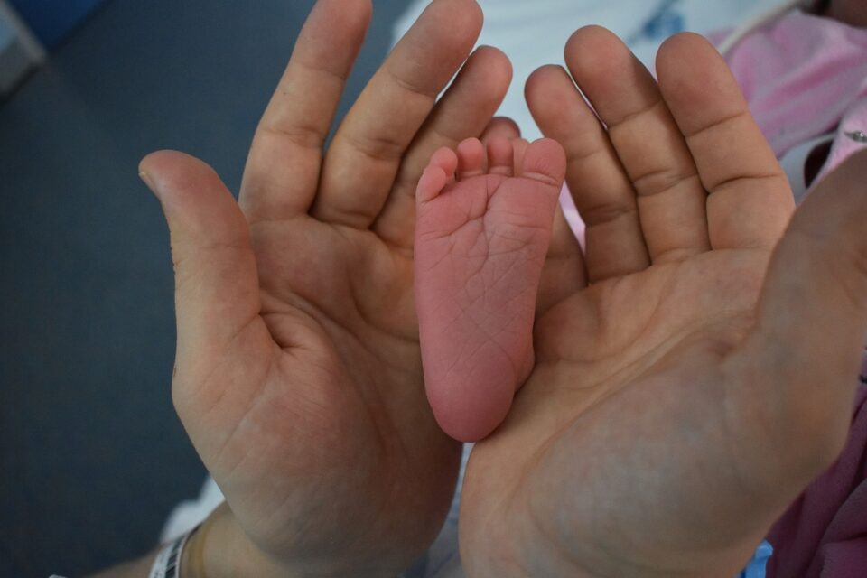 Mãos de um adulto seguram delicadamente o pé de um recém-nascido, simbolizando cuidado, proteção e vínculo familiar.