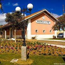 Prédio da antiga estação ferroviária de Maria da Fé, em Minas Gerais, com fachada cor de rosa, telhado de duas águas e jardim florido à frente, sob céu azul com poucas nuvens