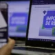 Tela de computador exibe página da Receita Federal com o título "Declaração de Imposto de Renda 2025", enquanto uma mão segura um celular com o aplicativo da Receita aberto em primeiro plano.