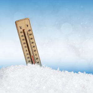 Termômetro de madeira fincado no gelo exibe temperatura negativa, simbolizando clima de frio extremo com fundo azul desfocado.