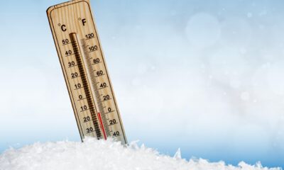 Termômetro de madeira fincado no gelo exibe temperatura negativa, simbolizando clima de frio extremo com fundo azul desfocado.