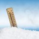 Termômetro de madeira fincado no gelo exibe temperatura negativa, simbolizando clima de frio extremo com fundo azul desfocado.