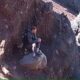 Homem ferido sentado sobre uma pedra, cercado por paredões rochosos, enquanto espera por resgate no Monte Rinjani.