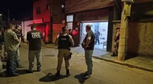 Agentes da Polícia Civil e Militar em frente a um salão de beleza iluminado, local do assassinato de um chefe do tráfico em Belo Horizonte.