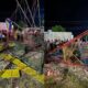 Imagem mostra os destroços de um brinquedo de parque de diversões, com ferragens retorcidas e assentos coloridos espalhados pelo chão. Populares observam o local do acidente à noite
