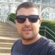 Homem de óculos escuros posando em frente a escadaria de estufa de vidro; identificado como Tiago Nicolau, vítima de ataque fatal em Leme, São Paulo