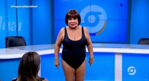 Personagem digital Marisa Maiô, criada por inteligência artificial, aparece em estúdio virtual vestindo maiô preto e falando com a plateia durante seu programa online