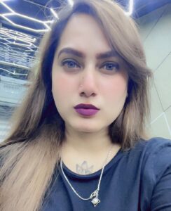 Retrato de Kanchan Kumari, influenciadora indiana de 30 anos, com cabelo castanho claro, batom roxo escuro e tatuagem visível no pescoço, tirado em ambiente moderno com luzes no teto