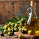 Garrafa de vidro com azeite extravirgem ao lado de ramos de oliveira e azeitonas verdes e pretas sobre uma tábua de madeira.