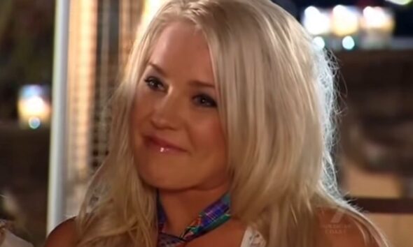 Tamika Chesser sorrindo em cena do reality show As Gostosas e os Geeks, com cabelo loiro solto e maquiagem leve.