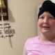 Garota sorridente usando turbante preto toca o sino da cura no hospital, com frase motivacional na parede ao lado, após vencer o câncer.