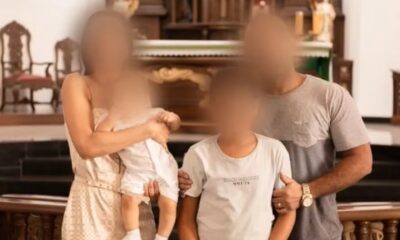 Foto de uma família composta por pai, mãe e dois filhos pequenos, com os rostos desfocados, posando juntos em frente a um altar de igreja.