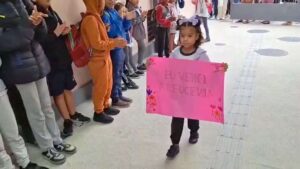 Menina chegando com cartaz escrito "Eu venci a leucemia"