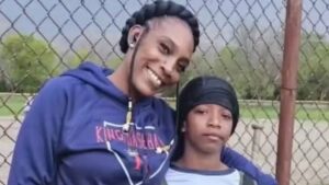 Mãe abraça o filho de 11 anos, ambos com roupas de frio, olhando para a câmera, ela sorri enquanto ele mantém expressão séria.