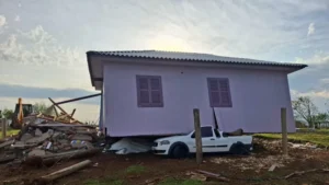 A imagem, fotografada durante o dia, traz uma casa que está em cima de uma caminhonete branca após forte temporal.