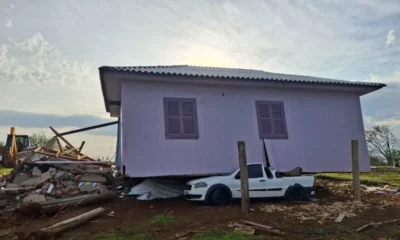 A imagem, fotografada durante o dia, traz uma casa que está em cima de uma caminhonete branca após forte temporal.