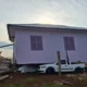A imagem, fotografada durante o dia, traz uma casa que está em cima de uma caminhonete branca após forte temporal.
