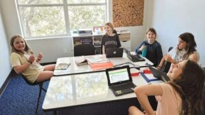 Alunos sentados em mesa com computadores