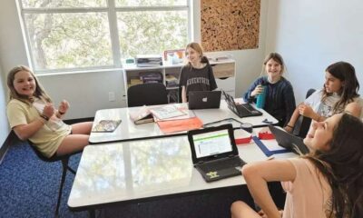 Alunos sentados em mesa com computadores