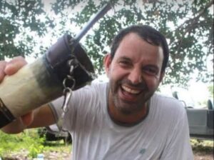 Piloto Marcelo Pereira de Barros está de blusa branca e sorrindo para a câmera. Ele segura uma cuia de chimarrão, bebida típica do Sul do Brasil.