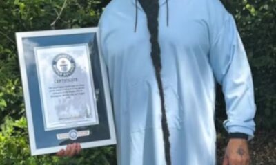 Homem negro com vestimenta azul e com a barba mais longa do mundo segurando o certificado do Guinness World Records.