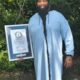 Homem negro com vestimenta azul e com a barba mais longa do mundo segurando o certificado do Guinness World Records.