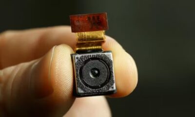 Imagem mostra uma mão segurando com o indicador e o polegar uma câmera pequena.