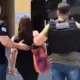 Foto mostra jovem sendo levada à delegacia por dois policiais.