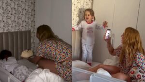Imagem mostra mãe sentada na cama com um bolo de aniversário entregando para sua filha de 3 anos.