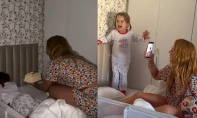 Imagem mostra mãe sentada na cama com um bolo de aniversário entregando para sua filha de 3 anos.