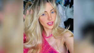 Mulher loira e de olhos azuis vestindo uma blusa rosa.