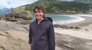 Imagem mostra homem com casaco preto em uma praia.