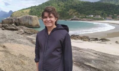 Imagem mostra homem com casaco preto em uma praia.